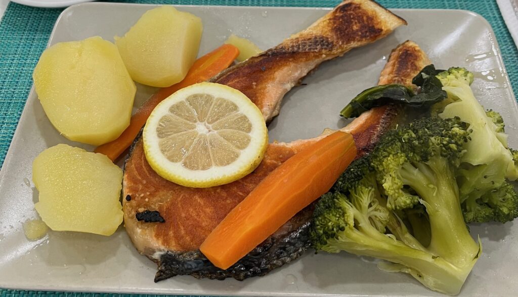 A posta de salmão (salmon steak) on a plate with boiled potatoes, broccoli, and carrot. There's a slice of lemon on top of the salmon.